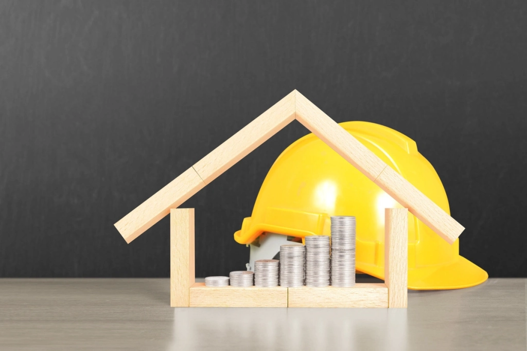 Pile de pièces avec une maquette de maison et un casque de chantier pour symboliser les travaux de rénovation